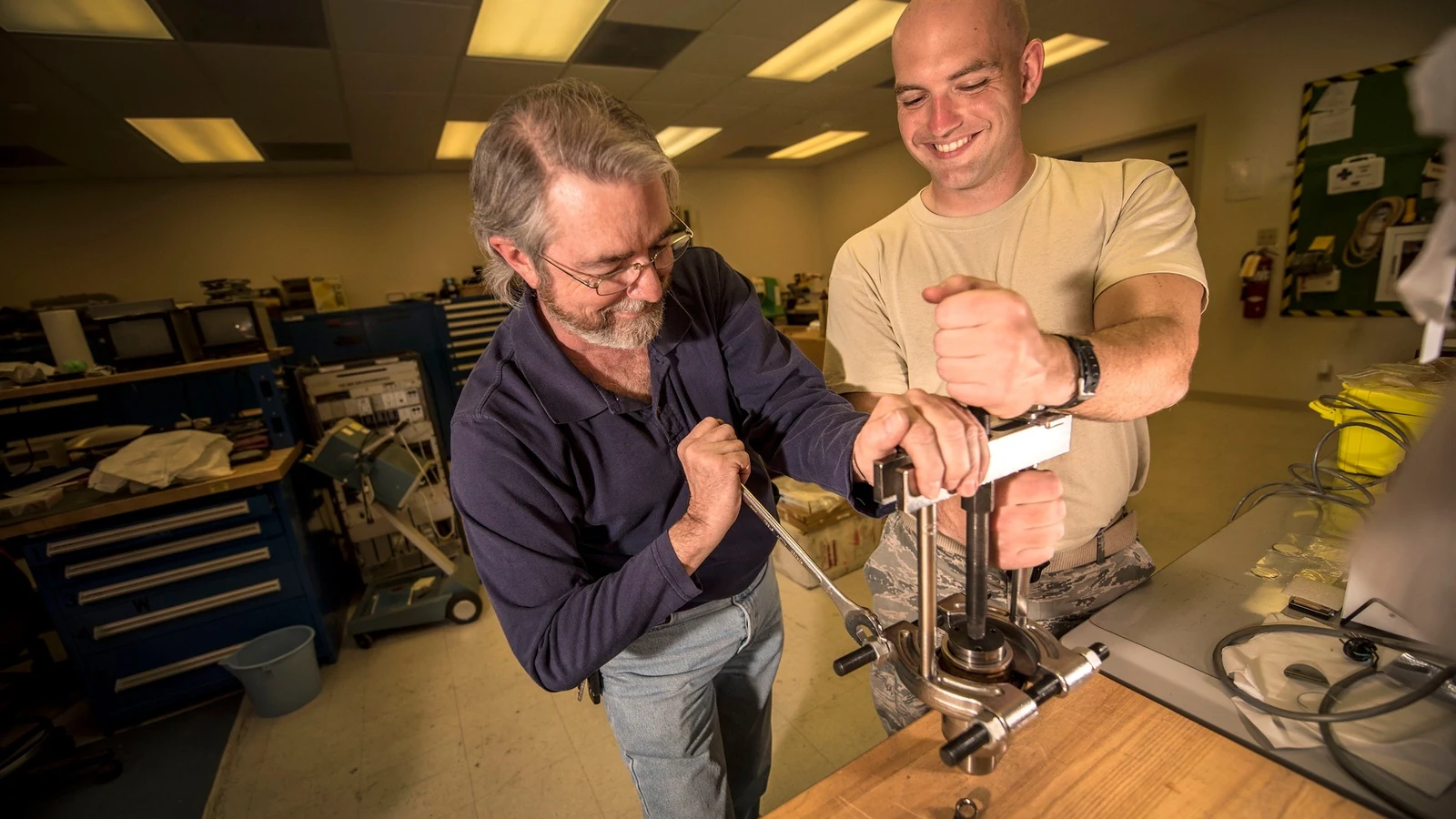 Two technicians work on the drive assembly of a large optical telescope.