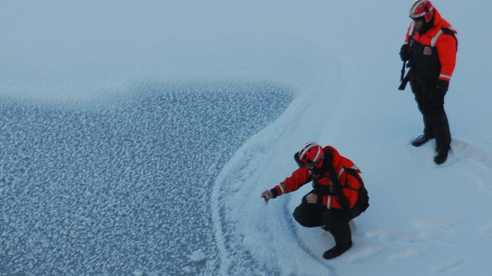 Two Coast Guard crew members conduct scientific observations on sea ice beside the cutter Healy.