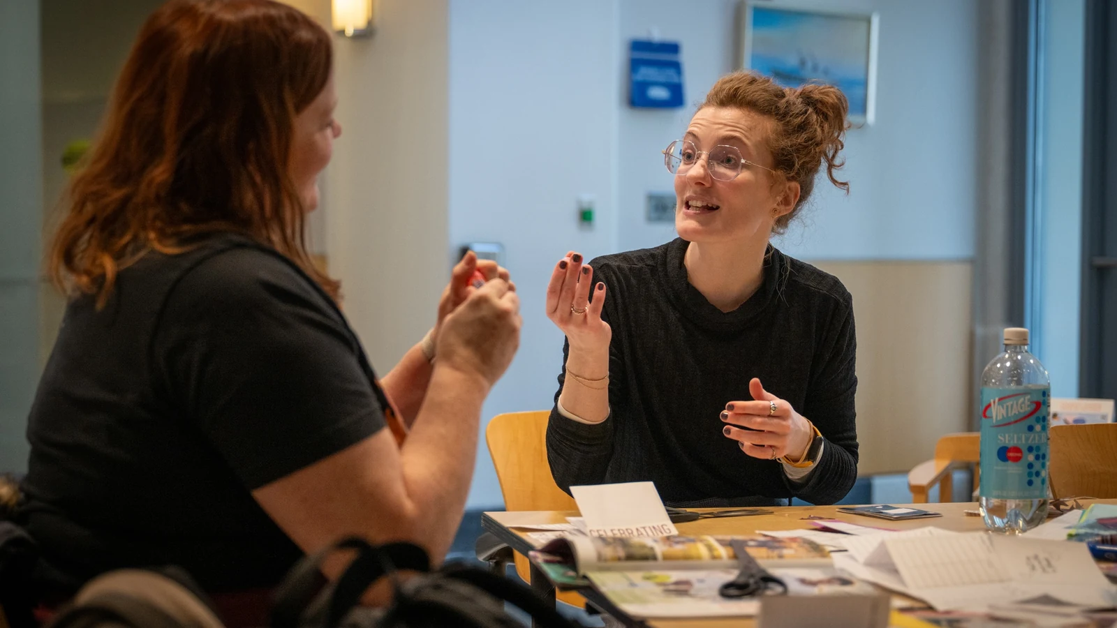 Two people smile and discuss books arranged on a table at a library event.