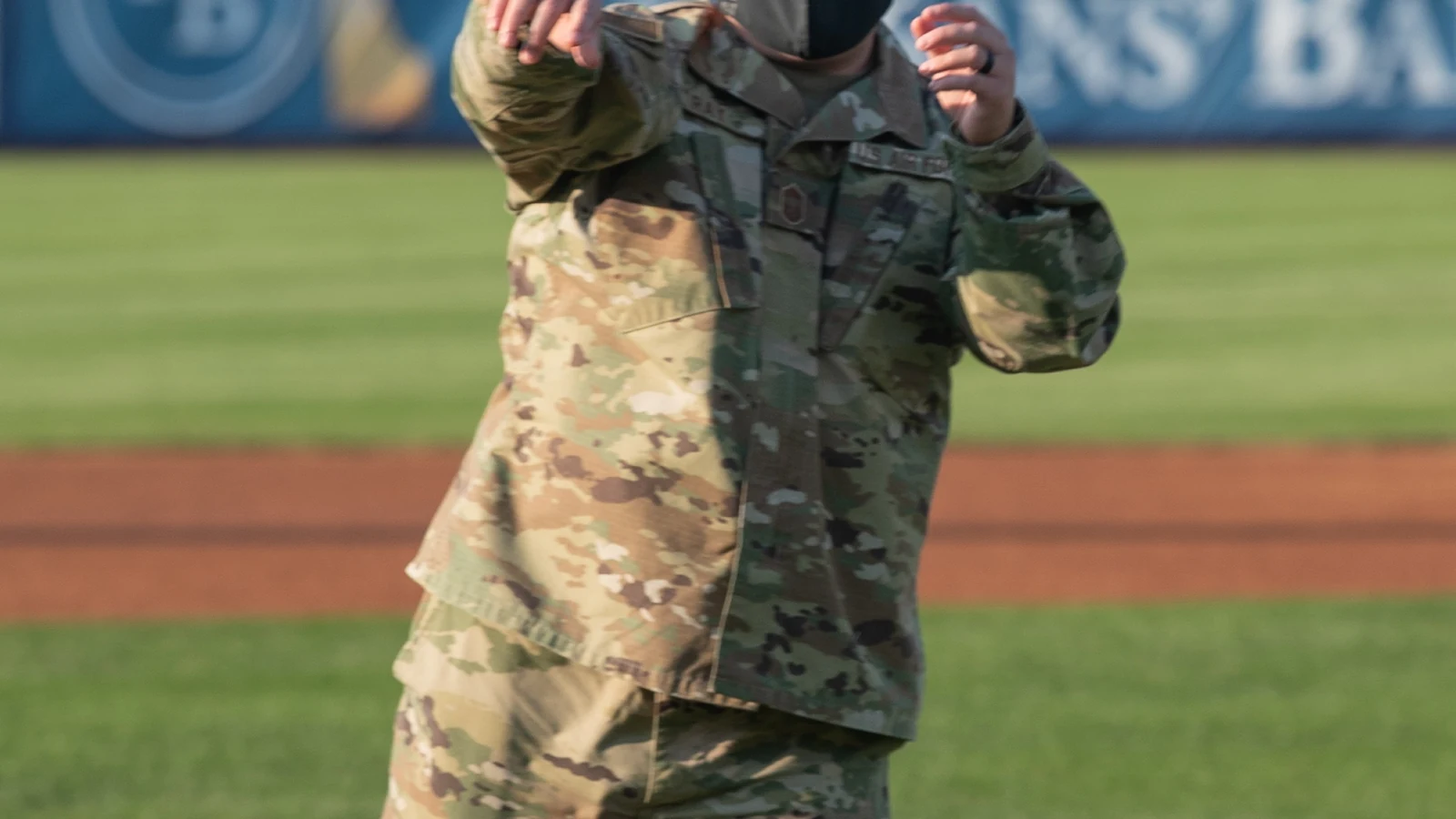 A uniformed service member throws a ceremonial first pitch from the mound at a baseball stadium.