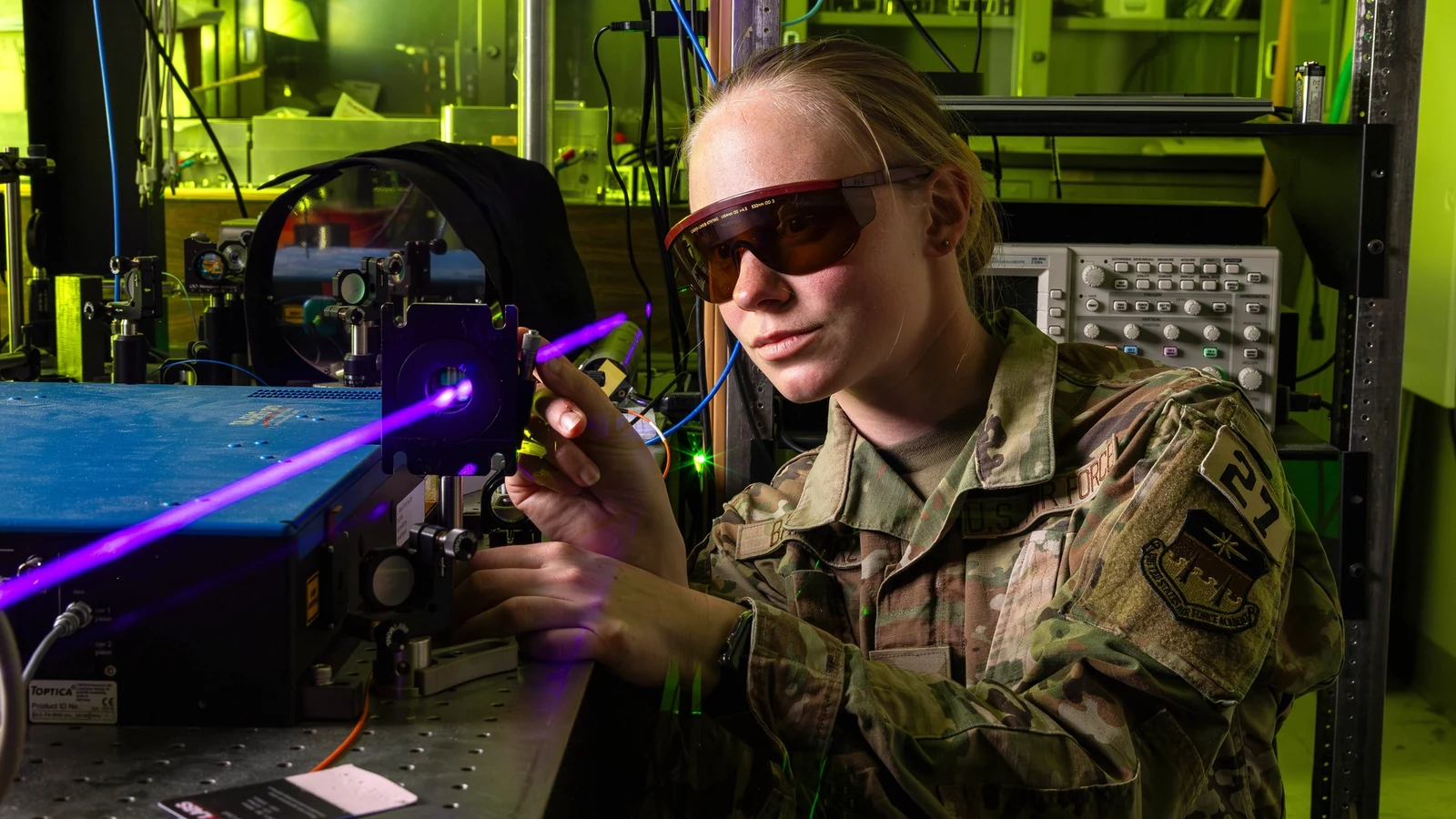 A scientist in protective glasses aligns a purple laser on an optical laboratory bench.