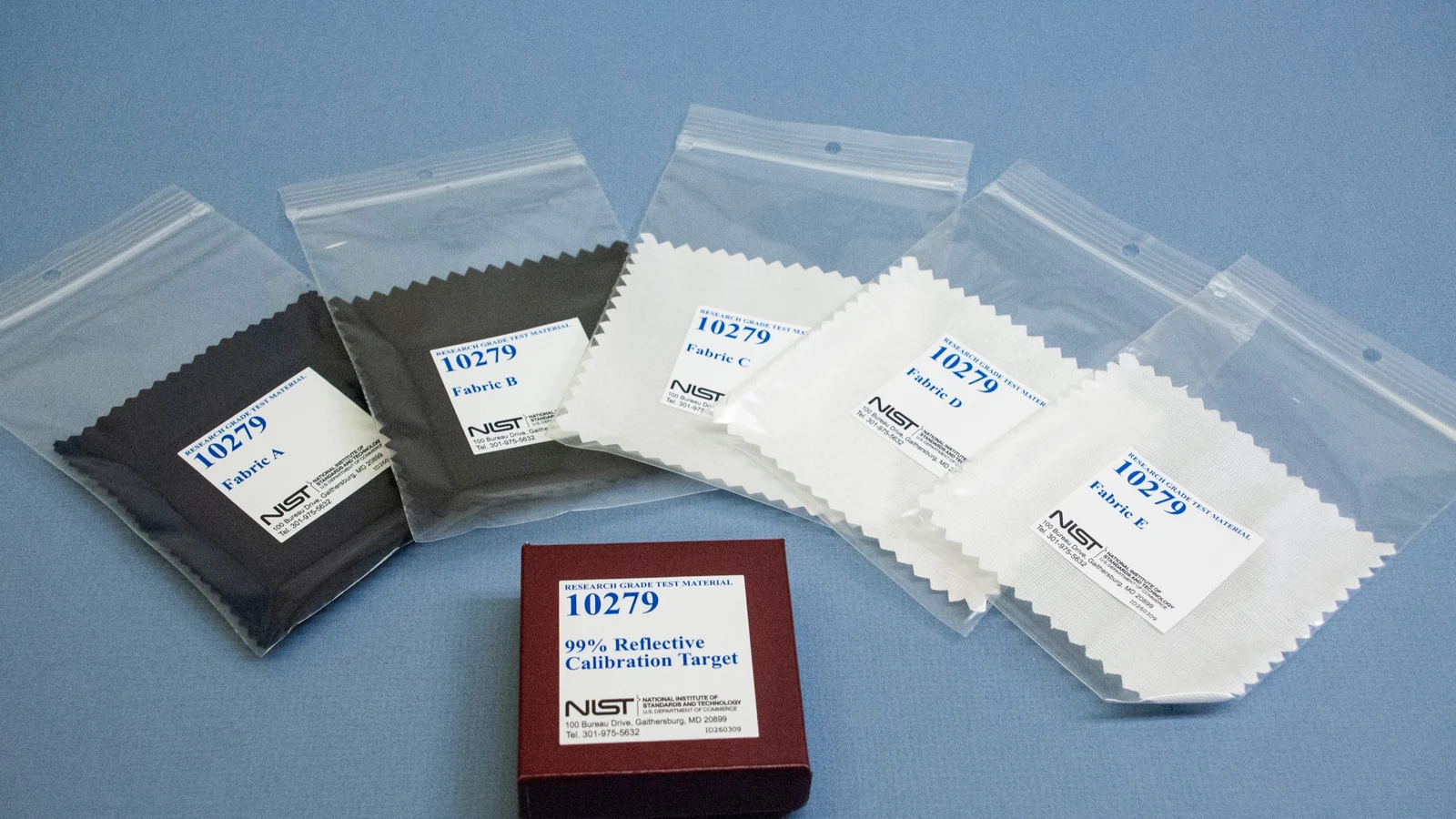 Five labeled fabric swatches arranged around a reflective calibration target on a blue surface.
