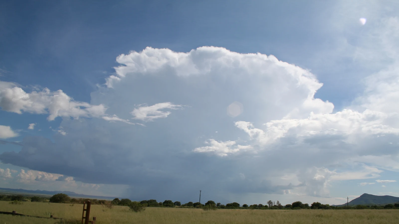 A dark summer thunderstorm builds over open grasslands beneath a broad desert sky.