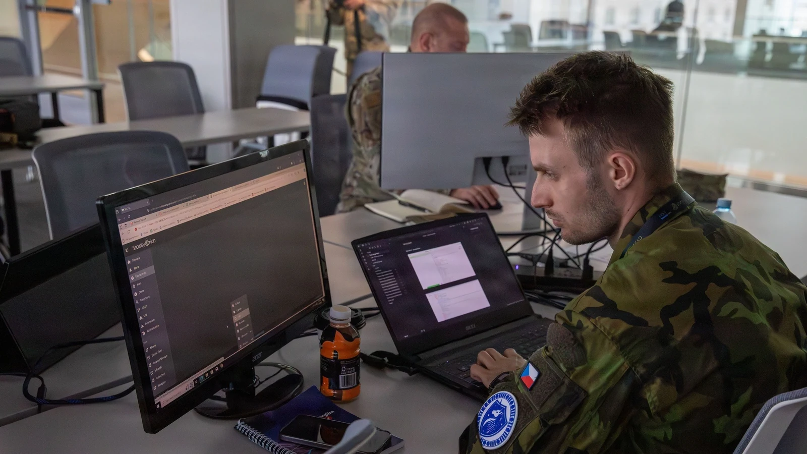 A cyber defender monitors simulated network systems across several computer screens.