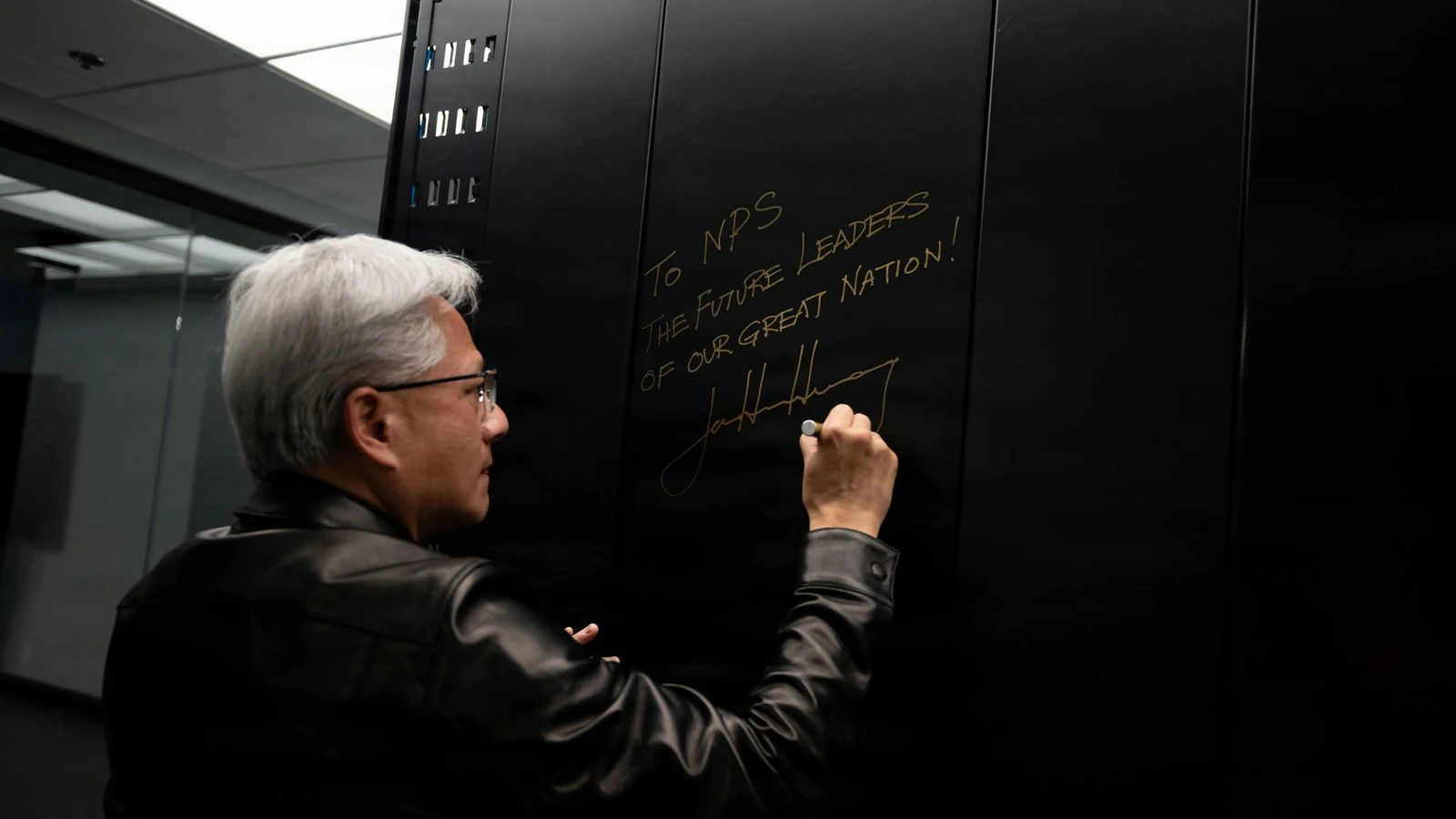 NVIDIA chief executive Jensen Huang writes a message on the black exterior panel of an AI supercomputer.