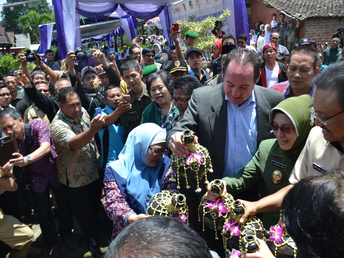 Adult community and government representatives cut a ribbon at the opening of a water and sanitation project in Indonesia.