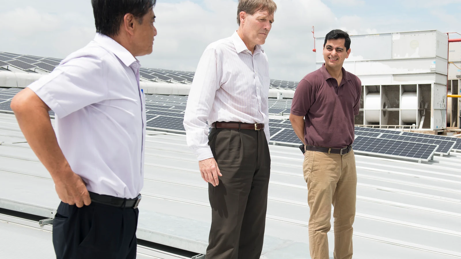 Adult officials in hard hats stand among rows of rooftop solar panels beneath a bright sky in Vietnam.