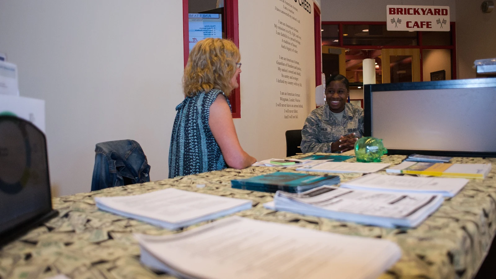 A financial counselor and an Airman sit across a desk discussing records on a laptop.