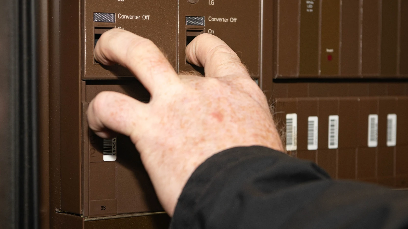 A technician reaches into a tall rack of telephone-switching equipment during its decommissioning.