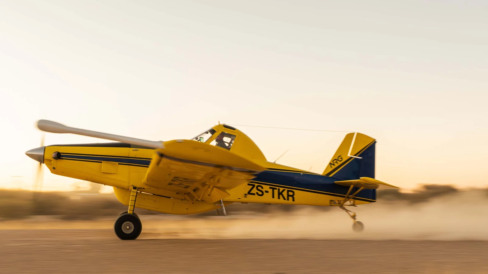 A yellow Air Tractor AT-504 survey aircraft accelerates along a runway at sunset.