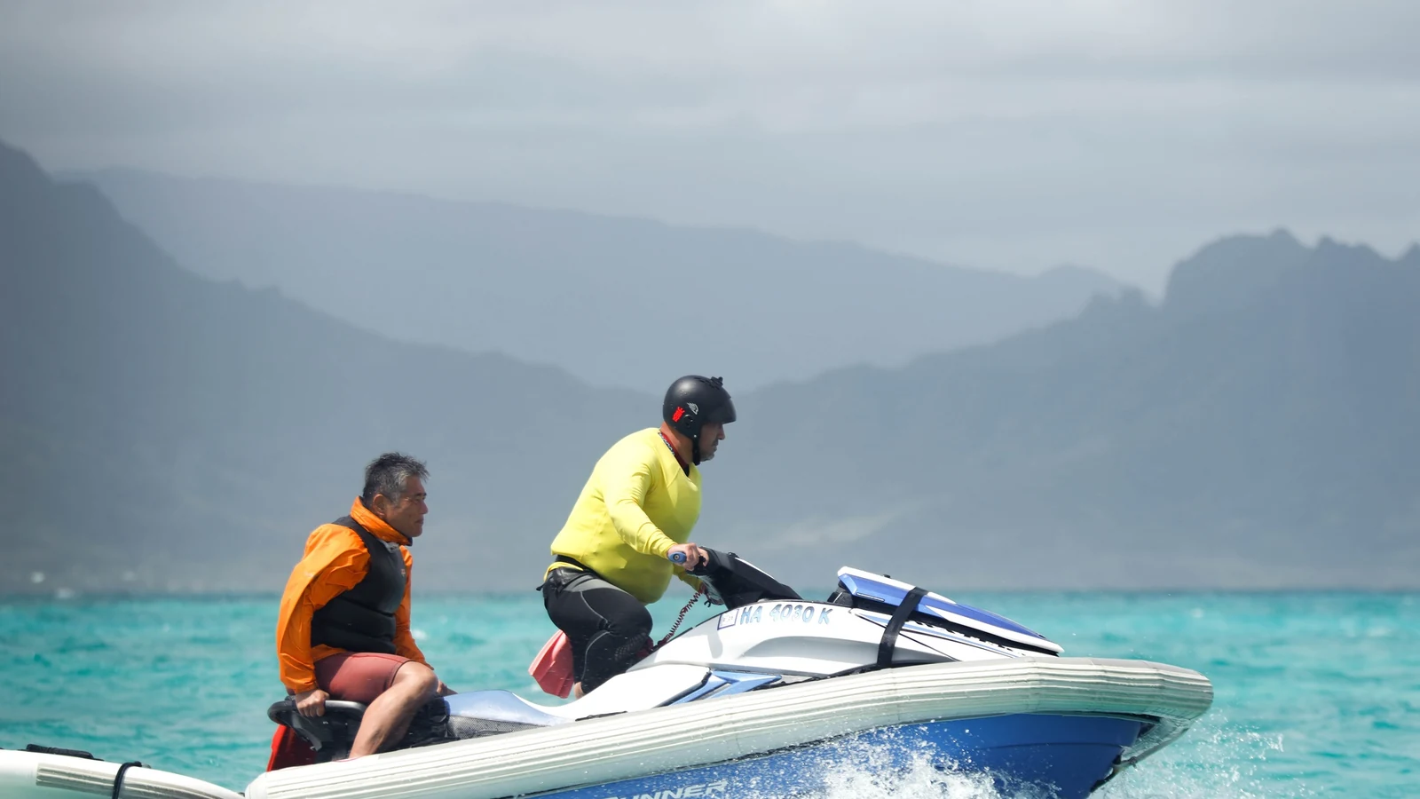 Two lifeguards operate a rescue watercraft through open water.