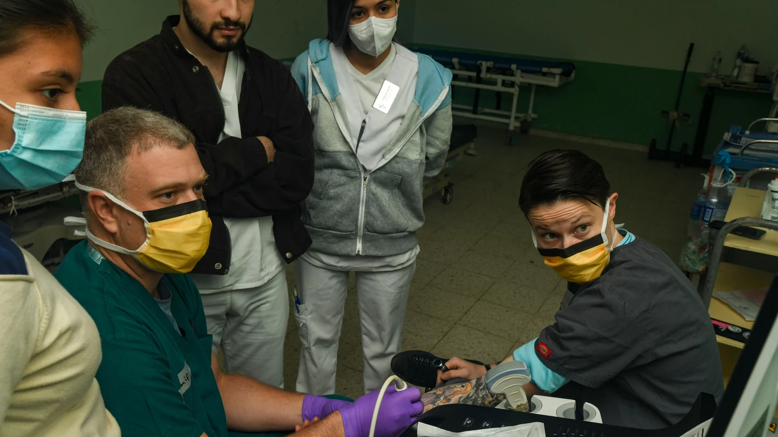 A nurse demonstrates ultrasound vein location to medical students in a hospital trauma bay.