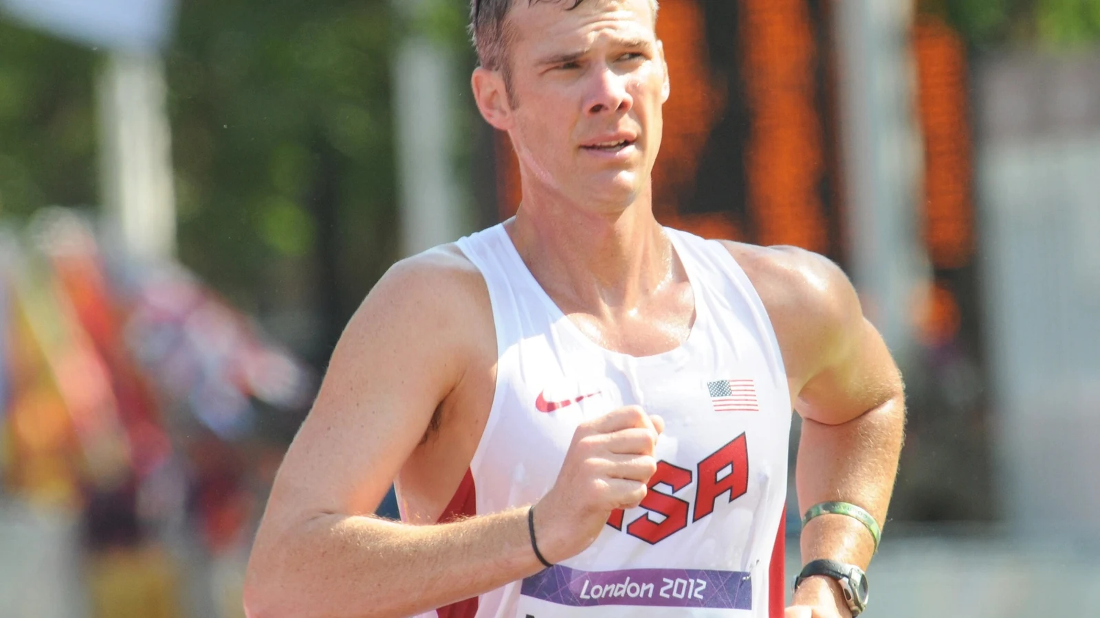 A race walker in a white uniform strides through a marked turn on a London course.