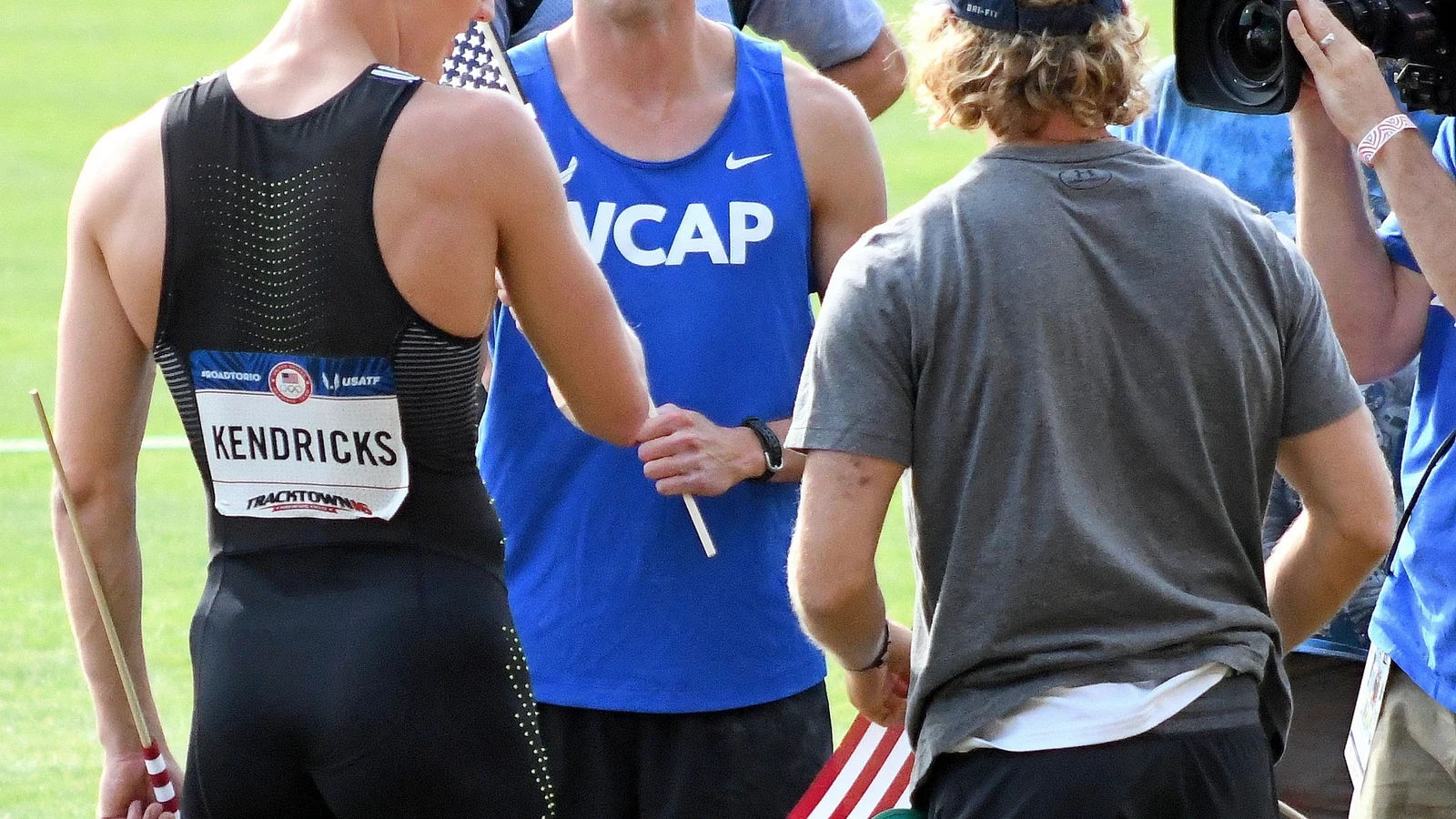 Three elite pole vaulters talk with staff beside the track after competition in Eugene, Oregon.