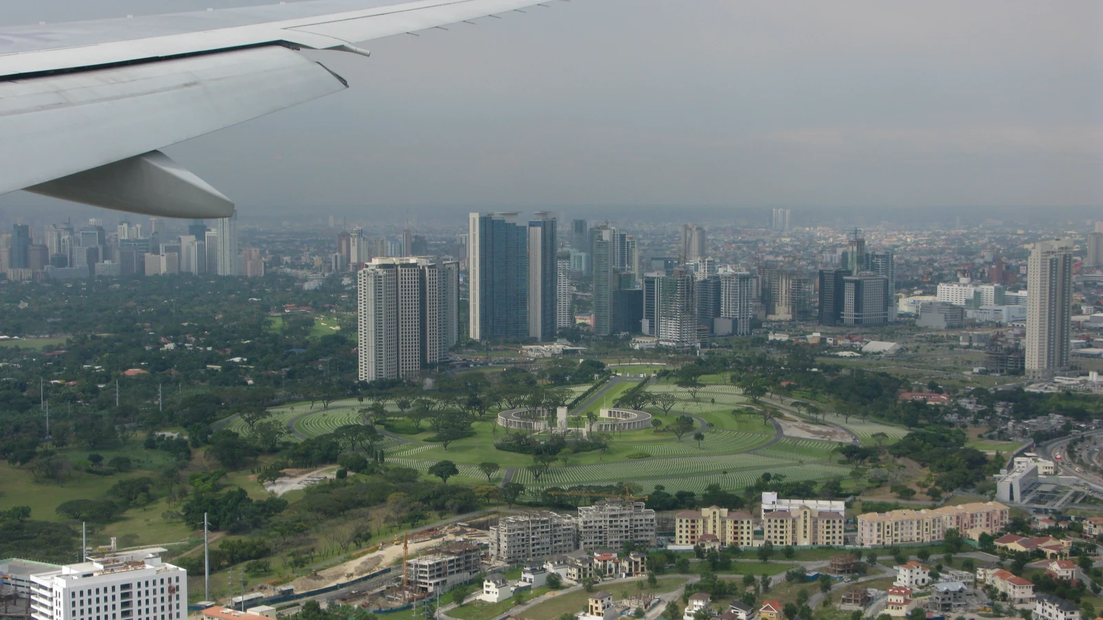 Aerial view of Manila’s dense skyline, roads and Manila Bay under scattered clouds.