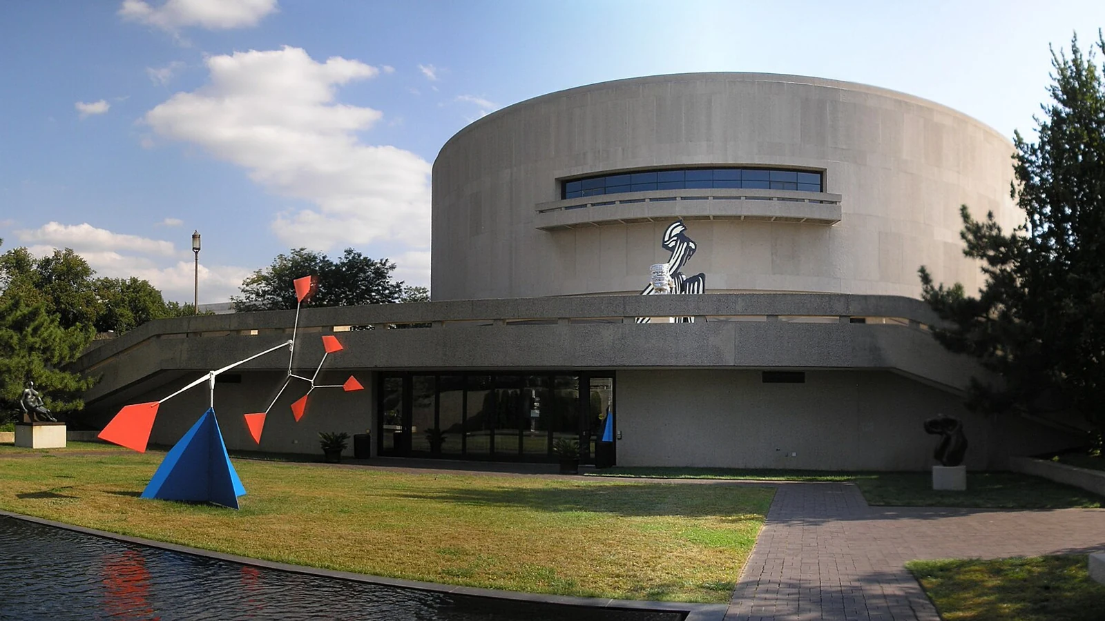 Modern sculptures stand on a green lawn in front of the circular Hirshhorn Museum in Washington.